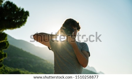 Low angle view of male photographer taking photo directly at you standing outside with rising sun glowing behind
him.