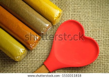 A flatlay picture of love and spices concept. Spices consist of chilli flakes, curry, India saffron, mix and coriander with heart shape wooden spoon.