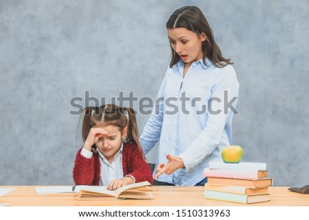 Mom and daughter on a gray background. At the same time mother quarrels with her daughter, shouts showing her index finger with an error. Schoolgirl cries ..
