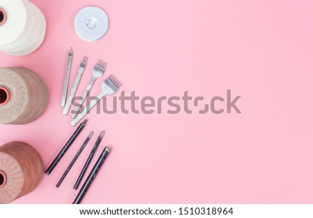 Top view with copy space of leather craft tools group, waxed rope, diamond hole punch and shape punch overhead on pink pastel background, Leather craft or leather working flat lay concept