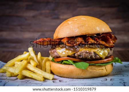 Craft beef burger with cheese, bacon, rocket leafs, caramelize onion and french fries on wood table and rustic background

