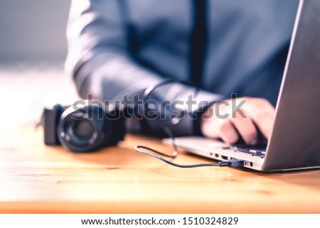 Camera connected to laptop with usb cable. Man editing photos with computer software. Photographer transfer files to computer from DSLR. Backup storage for images. Professional editor working.