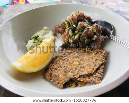 a white plate containing tuna and snacks mixed with sauce
