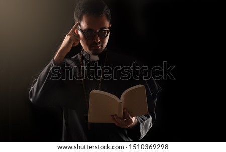 Dark tone, rim light - Priest point finger while holding bible on black background.  Think wisely,