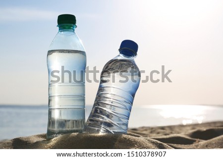 Sandy beach with bottles of refreshing drink on hot summer day, space for text