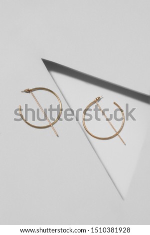 Closeup shot of metallic earrings made in the shape of golden open rings with long vertical pendants. The pair of earrings is isolated on the gray background with geometryc details. 