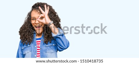 Young beautiful woman with curly hair wearing glasses doing ok gesture with hand smiling, eye looking through fingers with happy face.