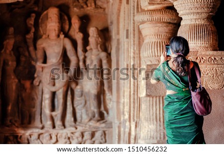 Woman making picture by smart phone inside the 6th century Hindu temple with caves. Carvings in ancient places India.