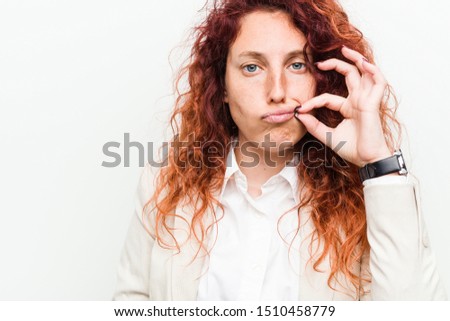 Young natural redhead business woman isolated against white background with fingers on lips keeping a secret.
