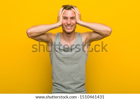 Young caucasian sport man laughs joyfully keeping hands on head. Happiness concept.