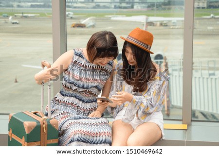 Two asian women using app on mobile phone, looking at screen of smart phone, texting, watching photos while traveling.