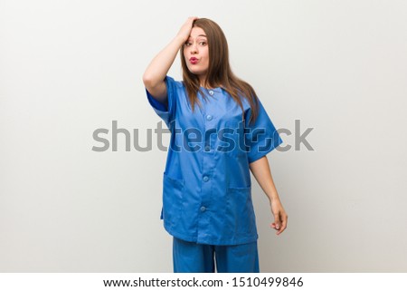 Young nurse woman against a white wall tired and very sleepy keeping hand on head.