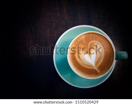 Coffee  Latte with Heart Design in green cup on wooden table in cafe with copyspace. Top view  on a rough textured wooden surface with dark vignetting and a highlight around the mug, 