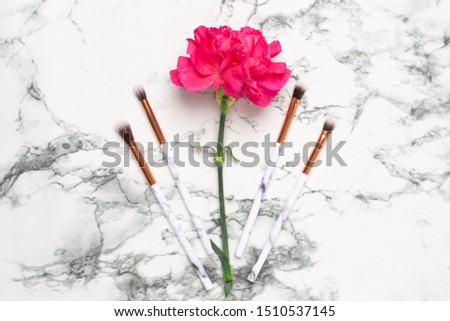 Beautiful pink flower with make up brushes on marble background top view