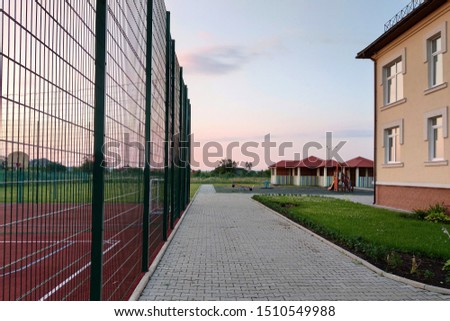 School of preschool building yard with basketball court surrounded with high protective fence.