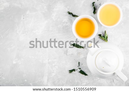 Herbal tea, cups and teapot with leaves on grey concrete background. Flat lay. 