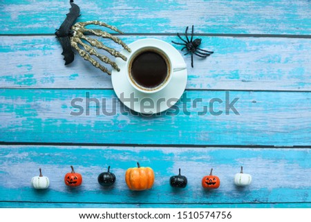 Background in Halloween concept. A cup of Americano coffee with hand bones, spider, bat and pumkins on the blue wooden background. Selective focus.  