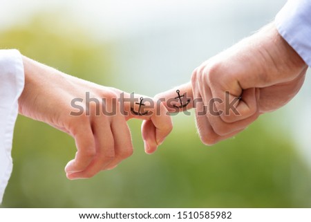 Loving Couple Holding Each Other's Finger With Black Anchor Sign Tattoo Against Blurred Background