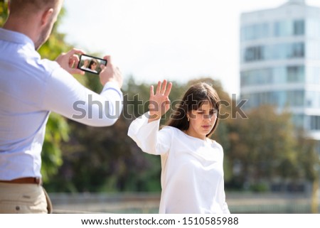 Young Woman Refusing  Man Taking Photo Of Her On Mobile Phone