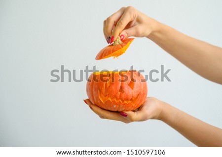 Female hands holding a pumpkin for Halloween. Close-up of a woman opens the jack-o'-lantern cover on a white background on the eve of all the saints. front view.
