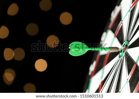 Green arrow hitting target on dart board against blurred lights. Space for text