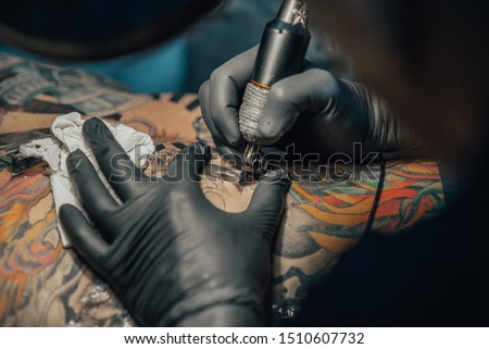 Close up of the tattoo machine. Tattooing. Man creating a picture on his back by a professional tattoo artist. Royalty-Free Stock Photo #1510607732