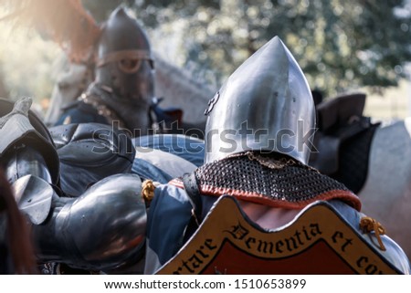 A knight in a helmet with a feather next to his horse. Reconstruction of the Middle Ages
