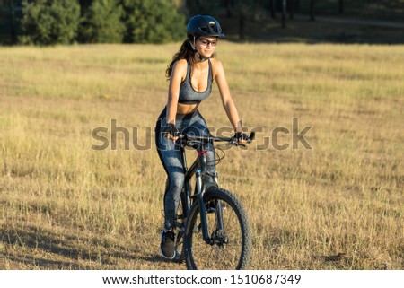 Girl on a mountain bike on offroad, beautiful portrait of a cyclist at sunset, Fitness girl rides a modern carbon fiber mountain bike in sportswear. The girl looks towards freedom and relaxation.