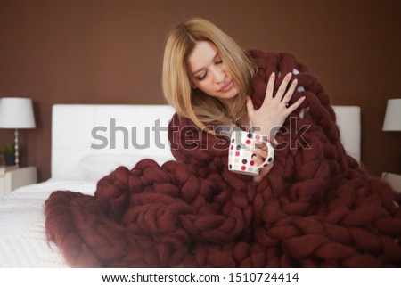 Happy young woman in Bathrobe sitting on bed wrapped in big and fluffy brown plaid. Beautiful girl in a cozy blanket with a Cup of drink. Warm and cozy at home, autumn mood