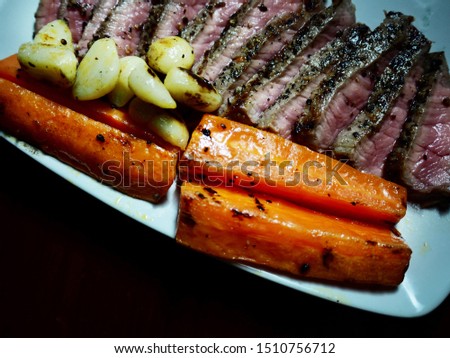 Close up picture of juicy medium beef rib eye steak slices with carrot and garlic on white plate isolated black background. Selective focus