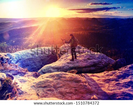 Lady photographer tourist with camera shoots sunrise while standing on top of the mountain.  Abstract filter.