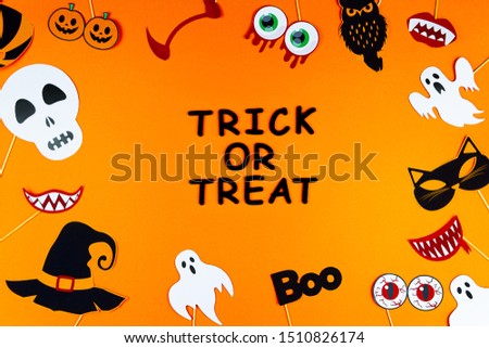 Funny paper photo props, 
photobuthoria, masks, are scattered in circle of canvas. Party accessories on orange background. Template for greeting card. Black inscription trick or treat. Happy halloween