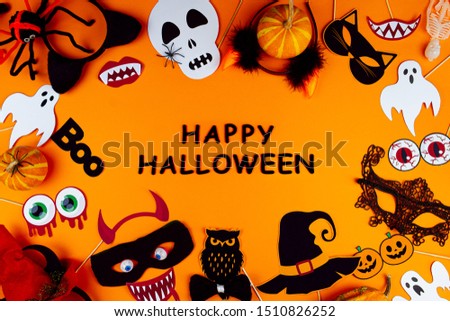 Little pumpkins, photo props, masks, decor for celebration are scattered in circle of canvas. Party accessories on orange background. Template for greeting card. Black inscription happy halloween.