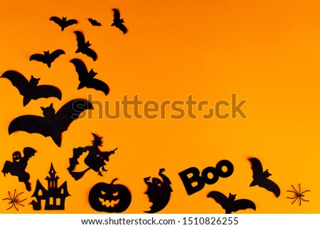 Black decorative paper figures photo props, masks are scattered on left side of canvas. Party accessories and decor for celebration on orange background. Template for greeting card. Happy halloween.