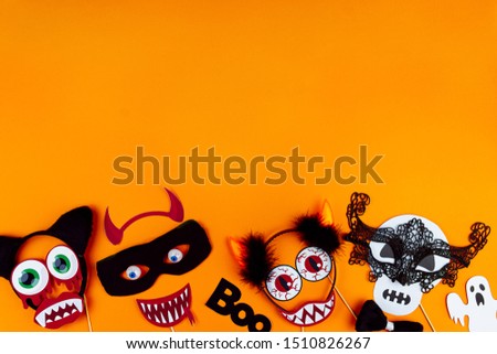 Funny faces of monsters are made of photo props, masks, headwear. Carnival supplies are scattered at bottom of canvas. Party accessories on orange background. Greeting card. Happy halloween.
