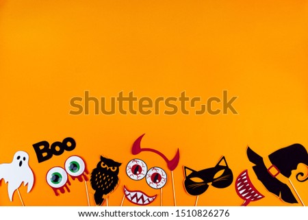 Funny faces of monsters are made of photo props. Photobuthoria, masks are scattered at bottom of canvas. Party accessories on orange background. Template for greeting card. Happy halloween concept.