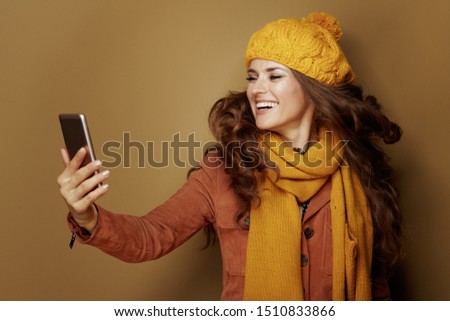 happy young woman in yellow beret and scarf taking selfie with phone and isolated on bronze background.