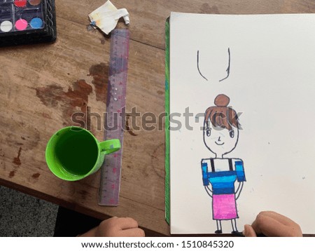 white sheet of drawing and school girl drawing close to the picture of her teacher in different colors, and a set of drawing on the wooden background.