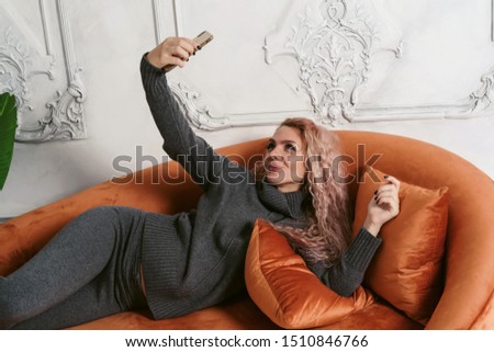 Young woman lying on her sofa taking a picture of herself at home in bedroom