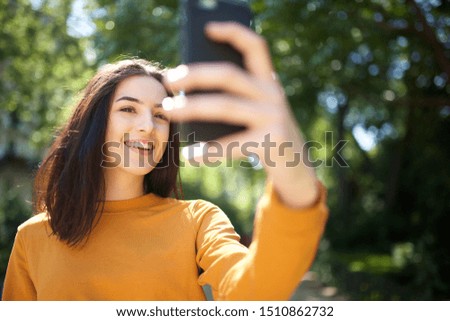 Portrait of happy young woman laughing in park while taking selfie