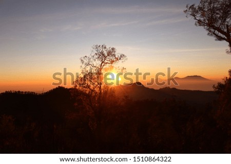 The rear lights of the sun rise in the mountain landscape with a large sun in the sky