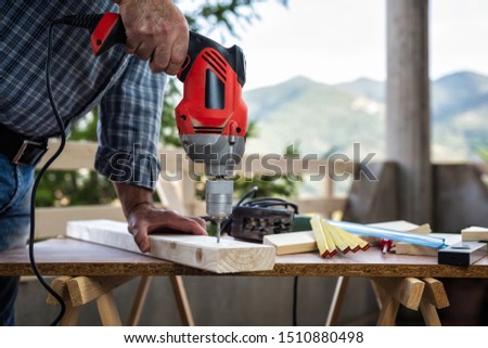 Adult craftsman carpenter with electric drill works makes a hole on a wooden table. Housework do it yourself. Stock photography.