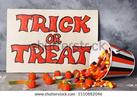 Text Trick or Treat with candies in bucket on grey background