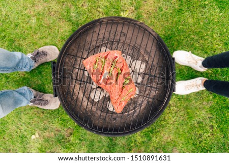 Flat lay picture of a real barbecue grill - top view of a couple cooking one big piece beef meat on a small round coal bbq