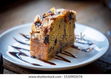 Banana cake with raisins, nuts and liquid chocolate on a white plate. The picture shows on an antique wooden table in a soft color by natural light from the window.