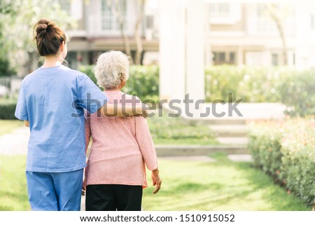 Back view of nurse caregiver support walking with elderly woman outdoor Royalty-Free Stock Photo #1510915052
