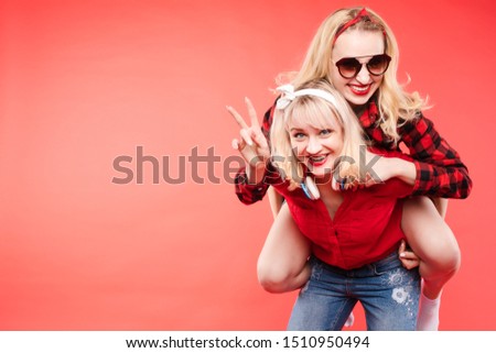 Friendly and trendy girls hugging over red background.