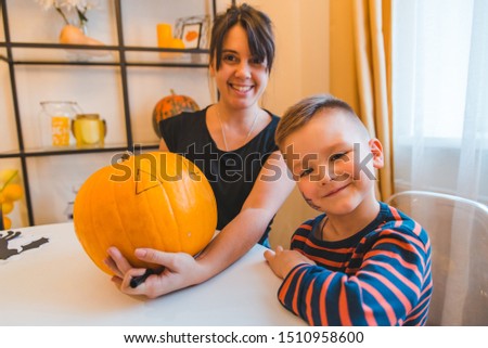 mother with son making pumpkin head at home together preparation to holiday little toddler boy