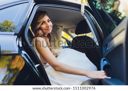 A bride takes pictures in the black car.