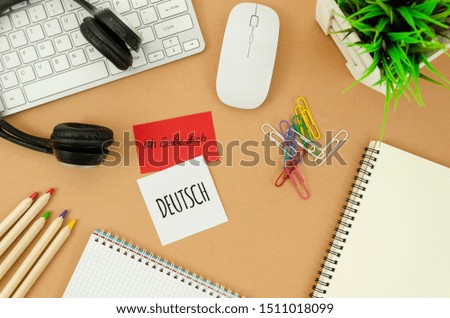 Flat lay desktop with blank spiral notepad, earphones, mouse, keyboard, and sticky notes with I love you sign on german. German learning concept